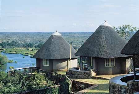 Thatched safari chalets overlook a winding river and the vast landscape in Kruger National Park.